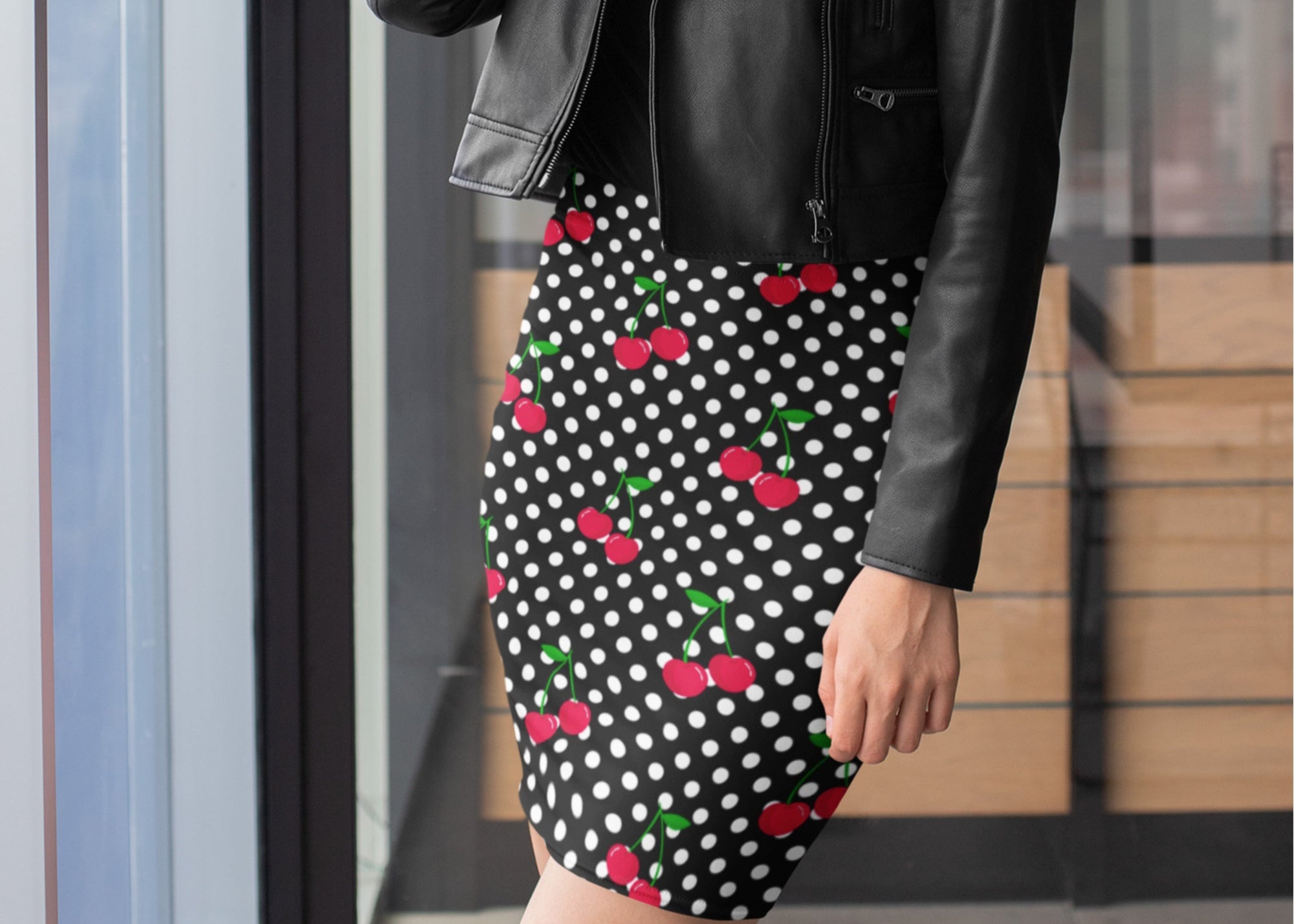 Person wearing a black leather jacket and polka dot skirt with red cherries.