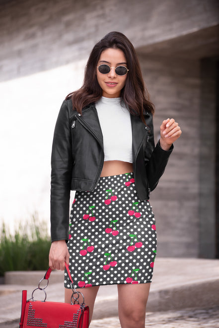Woman wearing a black leather jacket, white crop top, and polka dot skirt with red cherries.