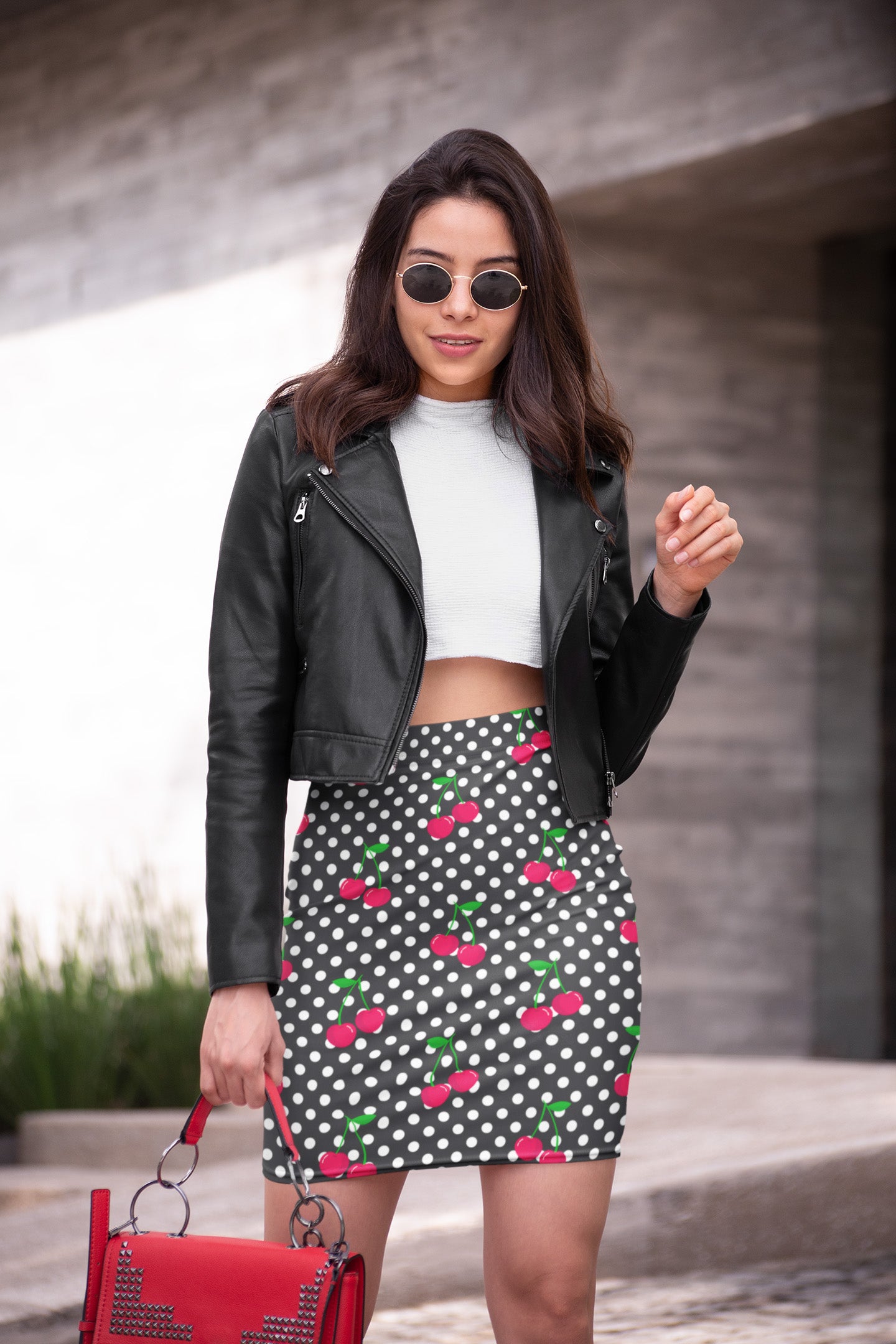 Woman wearing a black leather jacket, white crop top, and polka dot skirt with red cherries.