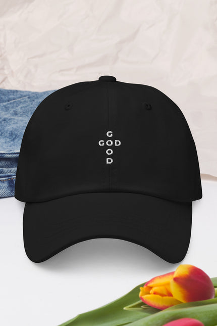 Black cap with 'G O D' is good  text, denim jeans, and tulips on a light background