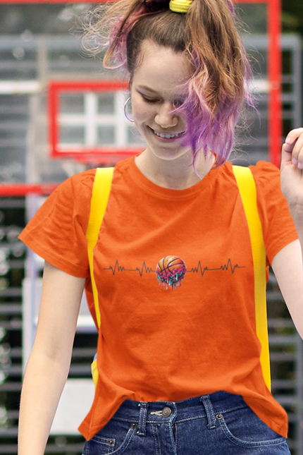 Person wearing an orange t-shirt with a colorful design, standing in front of a basketball hoop.