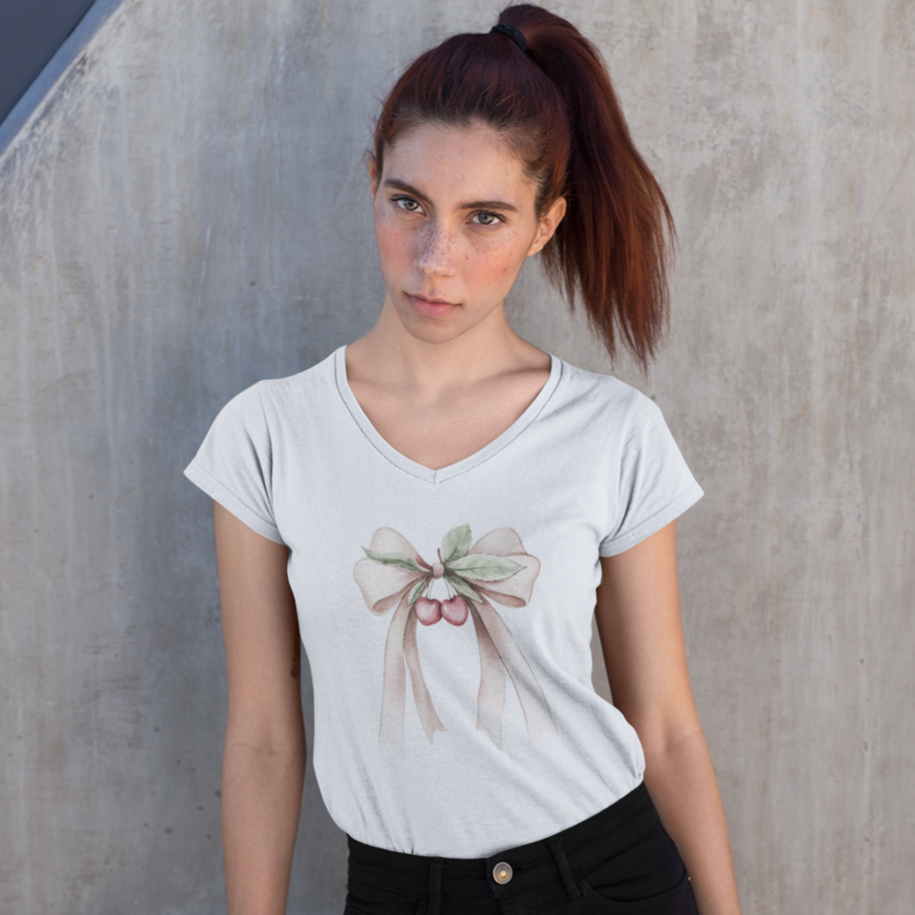 Woman wearing a white t-shirt with a graphic design against a concrete wall.
